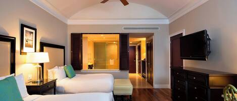 Une chambre d’hôtel avec deux lits, un ventilateur de plafond, une télévision, une commode et une vue sur le couloir.