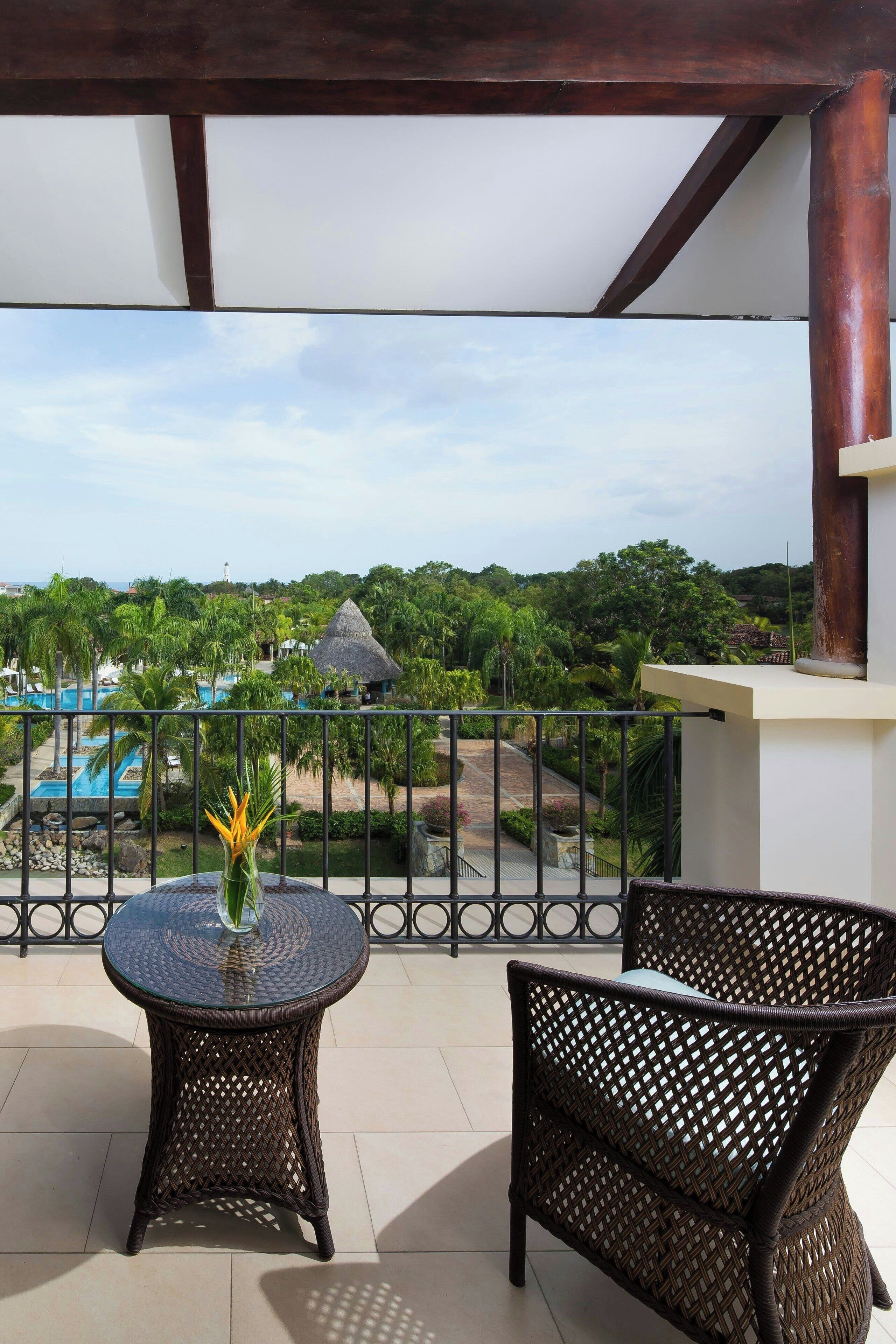 Un balcón con una mesa y una silla, con vistas a una piscina y abundante vegetación.