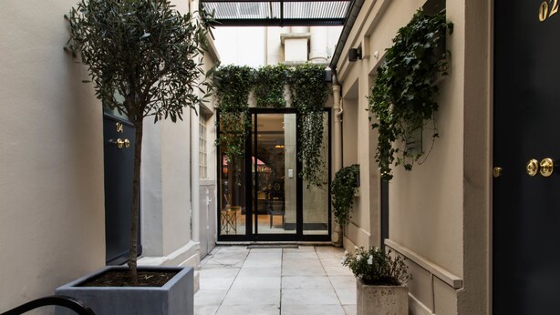 A narrow alleyway with a black door, potted plants, and a tiled floor.
