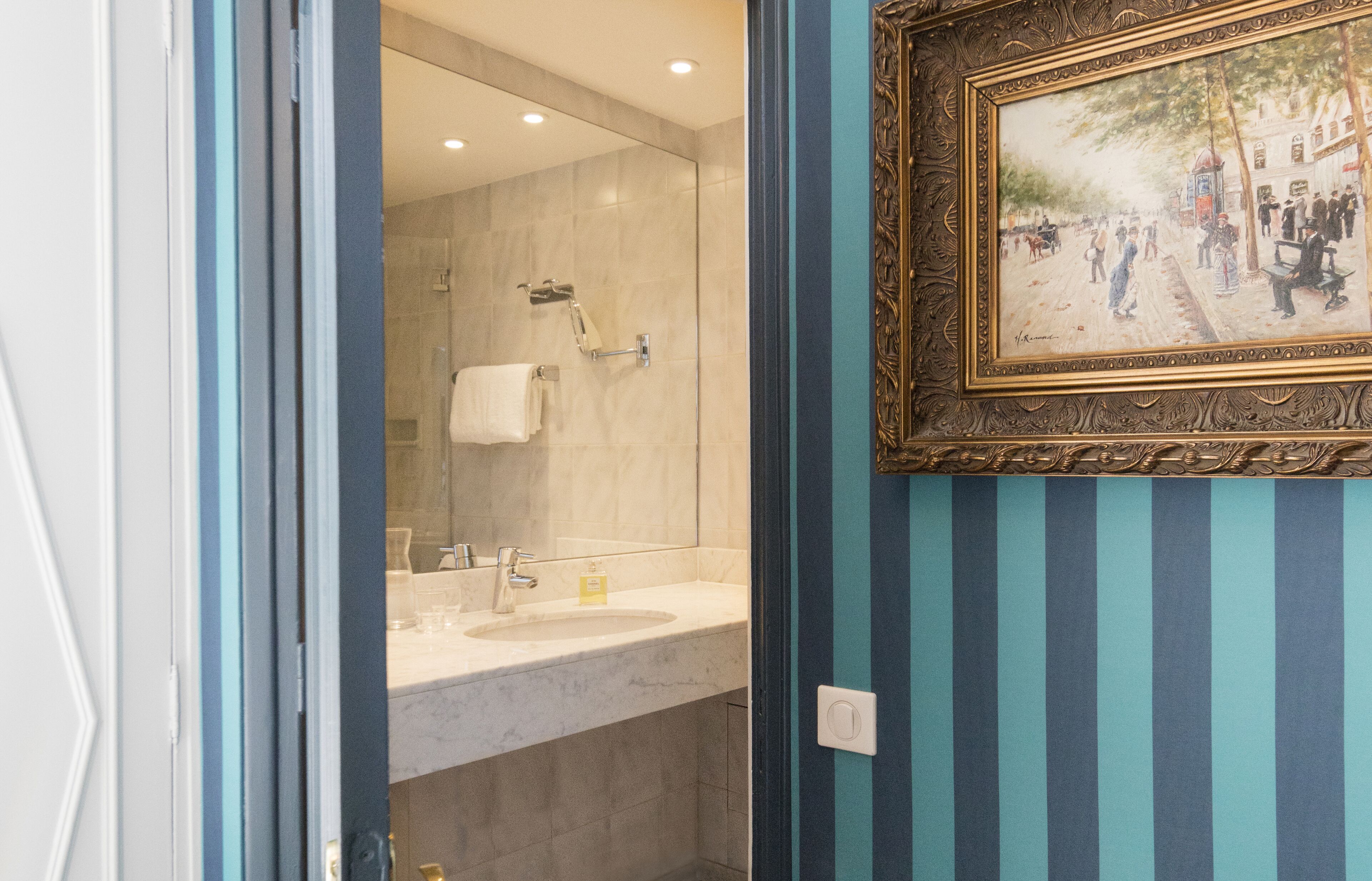 A bathroom with a marble sink, a shower, and a framed painting on the wall.