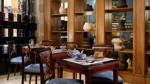 A dining area with wooden tables and chairs, a variety of pottery and decorative items on shelves, and a view of the street outside.