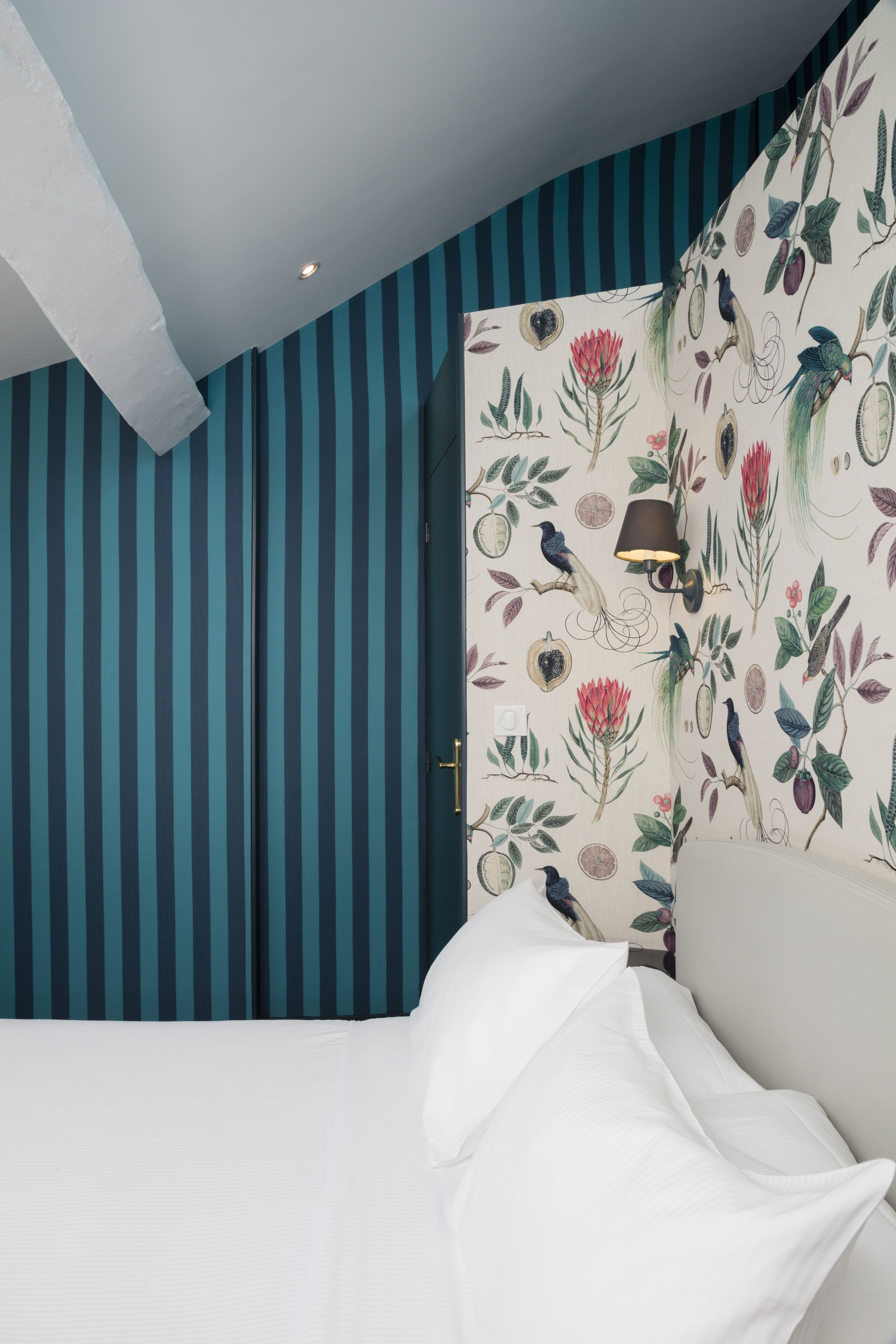 Una habitación con paredes a rayas, una cama con ropa blanca y una lámpara de pared.