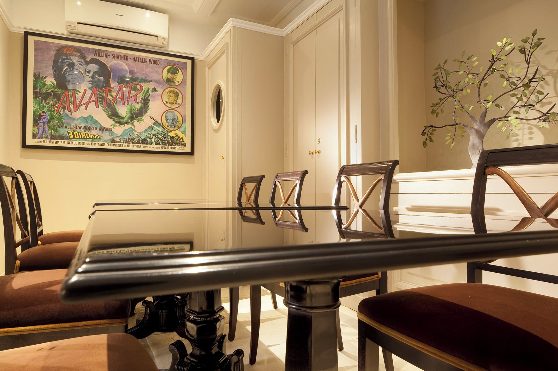 A dining area with a glass table, wooden chairs, and a framed movie poster on the wall.