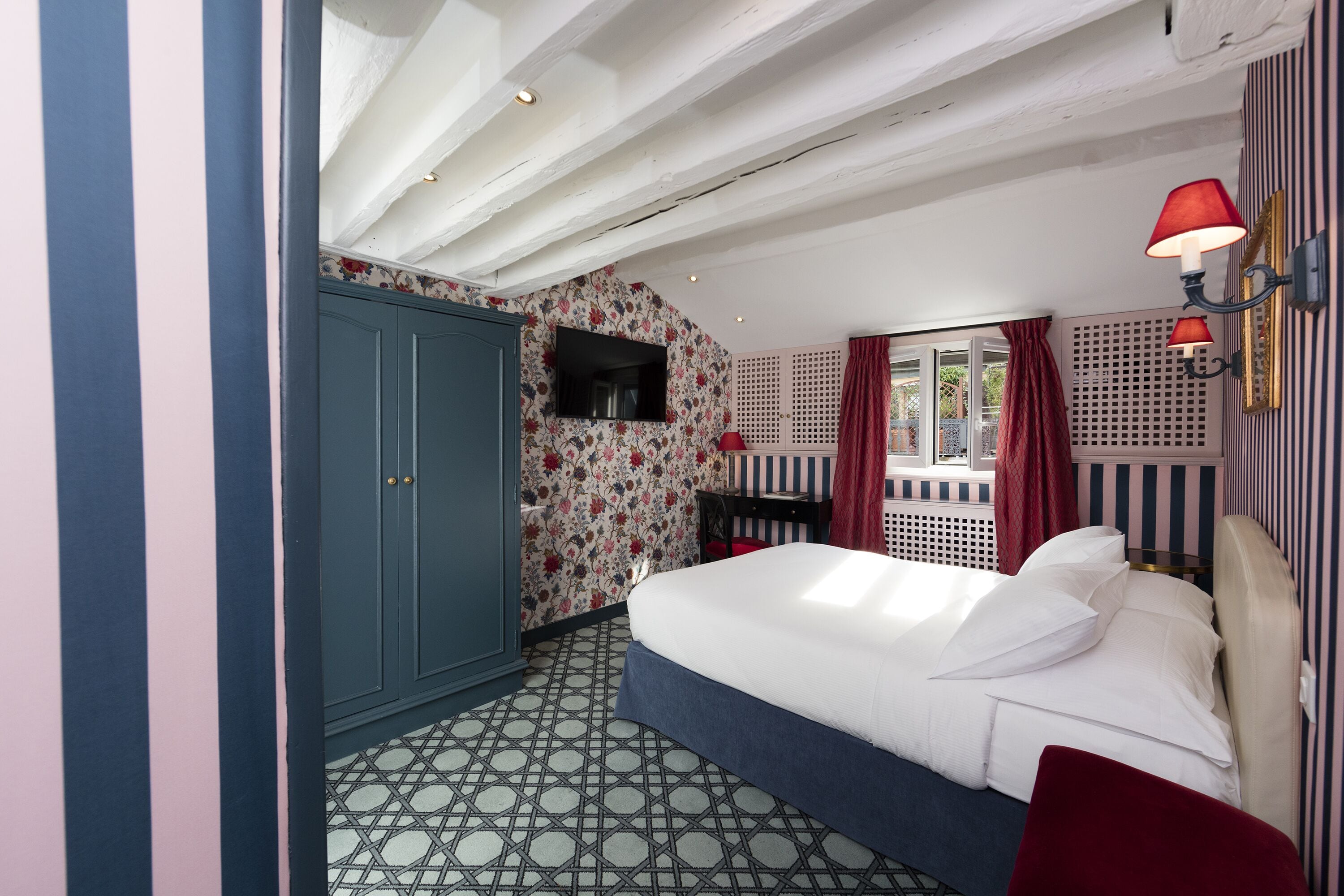 A bedroom with a large bed, a wardrobe, a TV, and a window with curtains.
