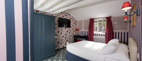 A bedroom with a large bed, a wardrobe, a TV, and a window with curtains.