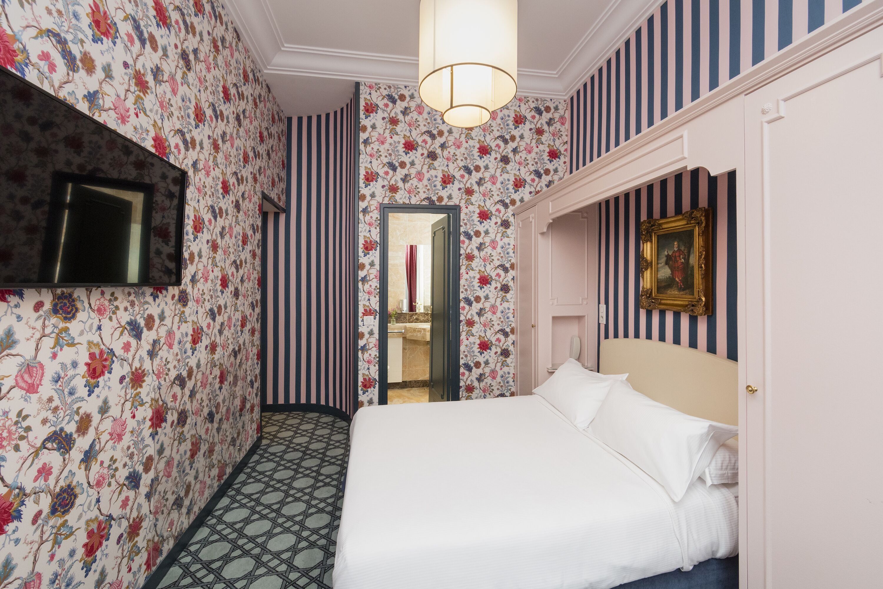 Une chambre d’hôtel avec un lit, une télévision, un miroir et un papier peint à rayures.