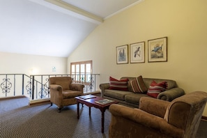 A cozy living room with a high ceiling, a balcony with a railing, and a sofa set.