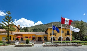 A hotel with a yellow facade, European flag, and a flag with a coat of arms.