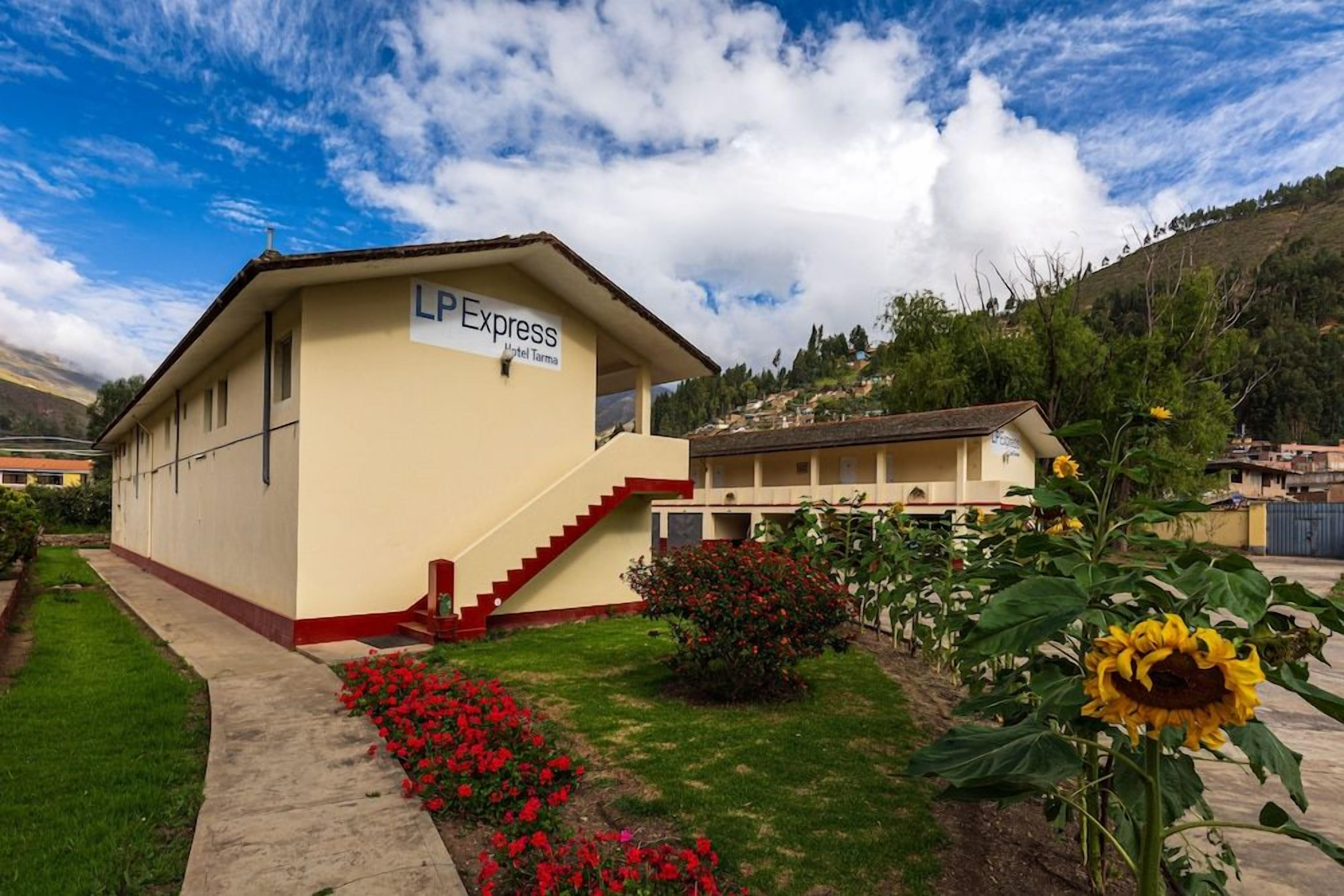 Un hotel llamado 'LP Express' con una escalera que conduce a la entrada, rodeado de un jardín con flores y un girasol grande.