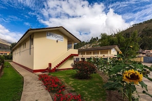 Un hotel llamado 'LP Express' con una escalera que conduce a la entrada, rodeado de un jardín con flores y un girasol grande.