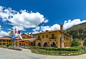 A yellow building with a red roof, multiple windows, and a flagpole with flags.