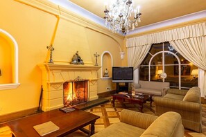A room with a fireplace, television, sofa, and a chandelier.