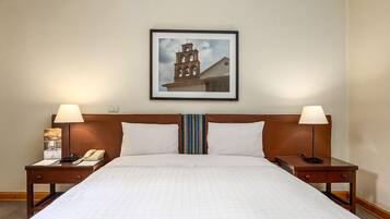 Habitación de hotel con una cama grande, dos mesitas de noche con lámparas, un cuadro enmarcado en la pared y un teléfono sobre una de las mesitas.
