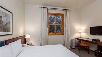 Habitación de hotel con cama, escritorio, silla, televisor y ventana con cortinas.