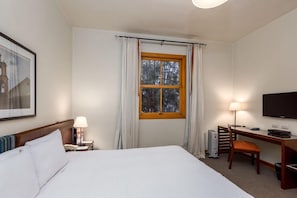 A hotel room with a bed, a desk, a chair, a television, and a window with curtains.