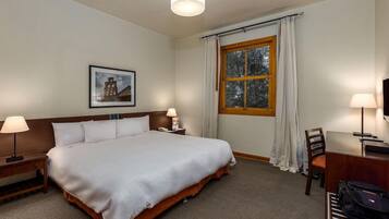 Habitación de hotel con cama, lámparas de noche, escritorio con silla, ventana con cortinas e imagen enmarcada en la pared.