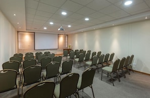 A conference room with rows of chairs, a projector screen, and a podium.