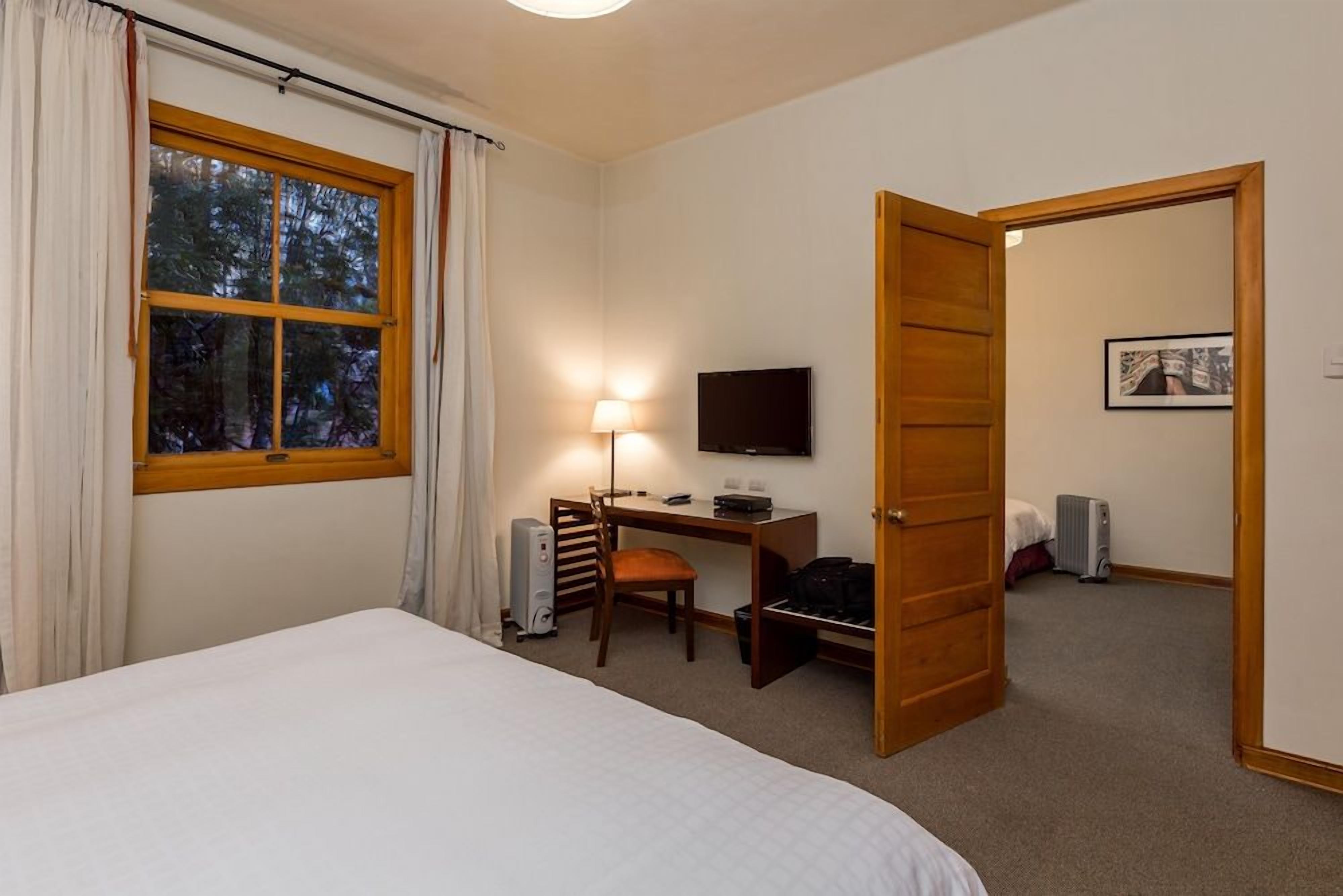 A hotel room with a bed, desk, chair, television, and a door leading to another room.
