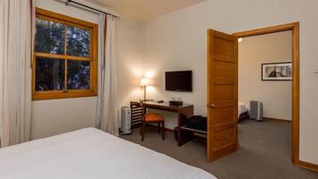A hotel room with a bed, desk, chair, television, and a door leading to another room.