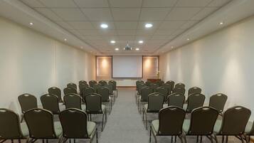 A conference room with rows of chairs facing a projection screen, a podium, and a carpeted floor.