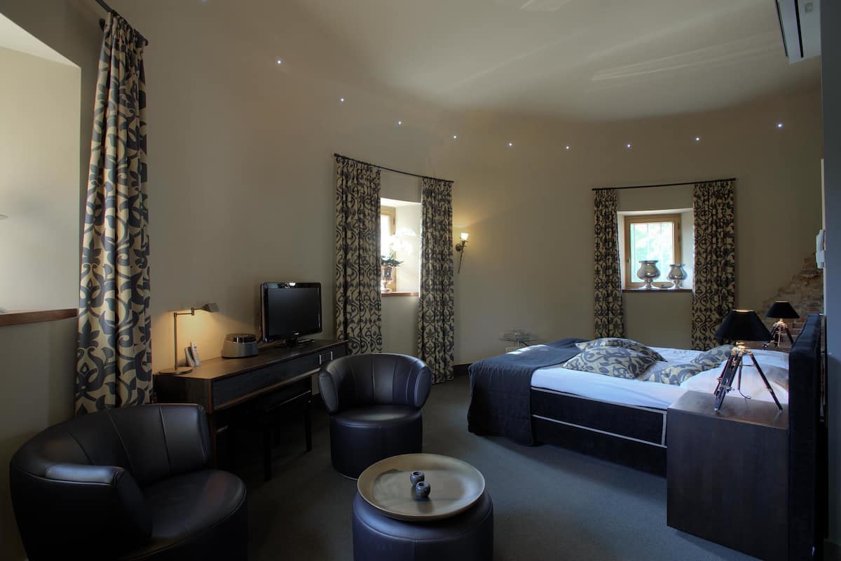 Une chambre d’hôtel comprenant un lit, un bureau avec une télévision, deux chaises, une petite table et des rideaux.
