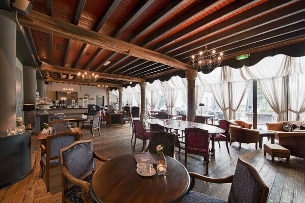 A restaurant with wooden beams, chandeliers, and a mix of wooden and upholstered chairs.
