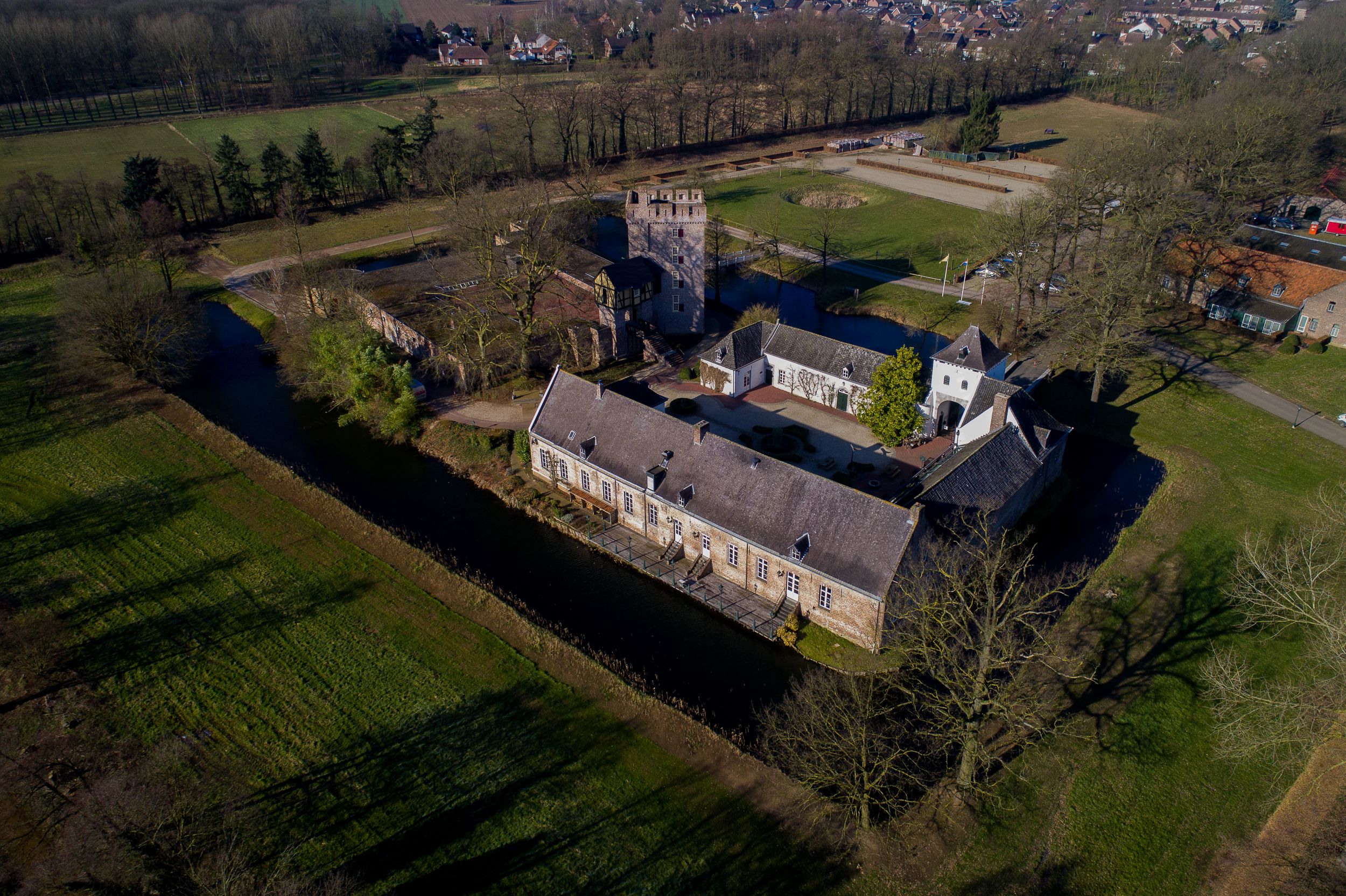 An aerial view of a historic building complex with a large central structure, a smaller tower, and a surrounding moat.