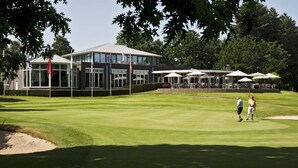 Un campo de golf con un club de campo que cuenta con amplios ventanales y terraza.