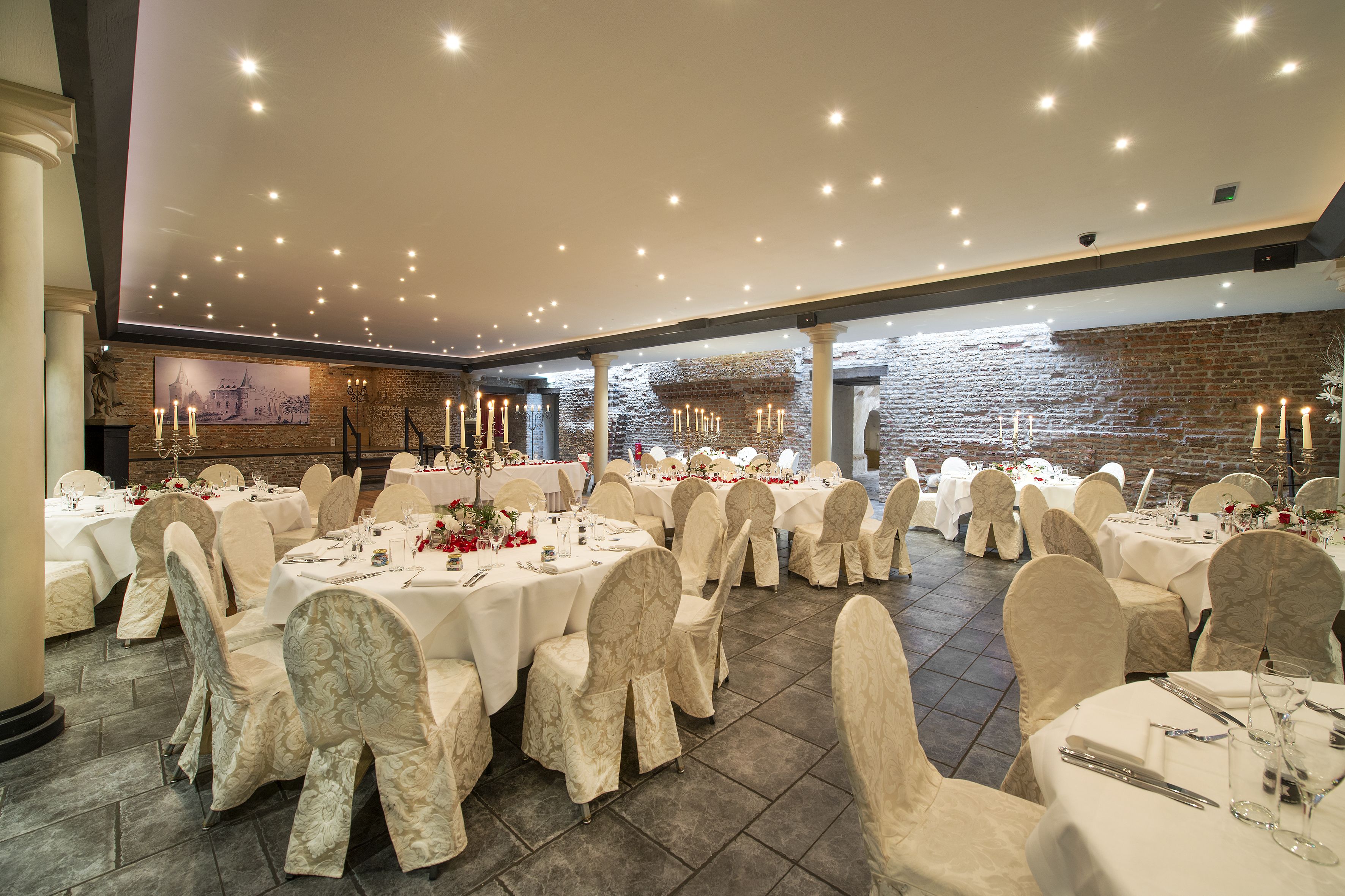 Un salón de banquetes con mesas redondas, manteles blancos y sillas con fundas estampadas.