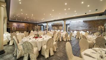 Un salón de banquetes con mesas redondas, manteles blancos y sillas con fundas estampadas.