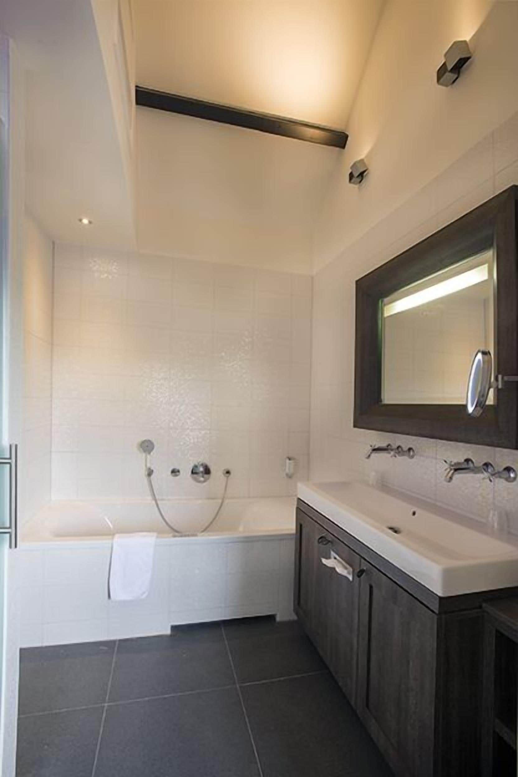 A modern bathroom with a bathtub, a vanity with a mirror, and dark wooden cabinets.