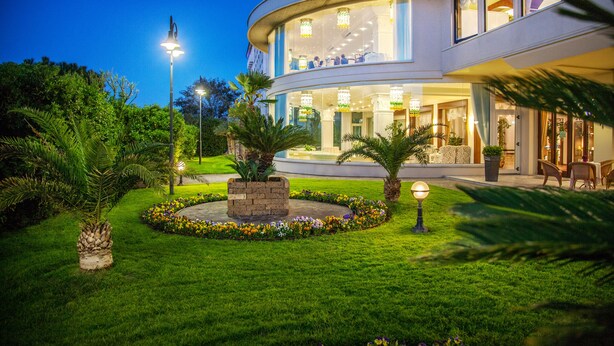 A modern hotel with a curved facade, outdoor seating, and well-maintained gardens. - Grand Hotel Gallia (Cervia)