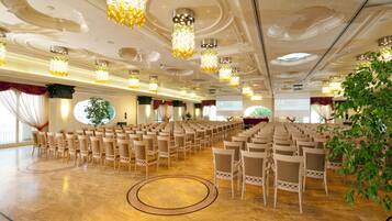 A conference room with rows of chairs, a stage, and a large screen.