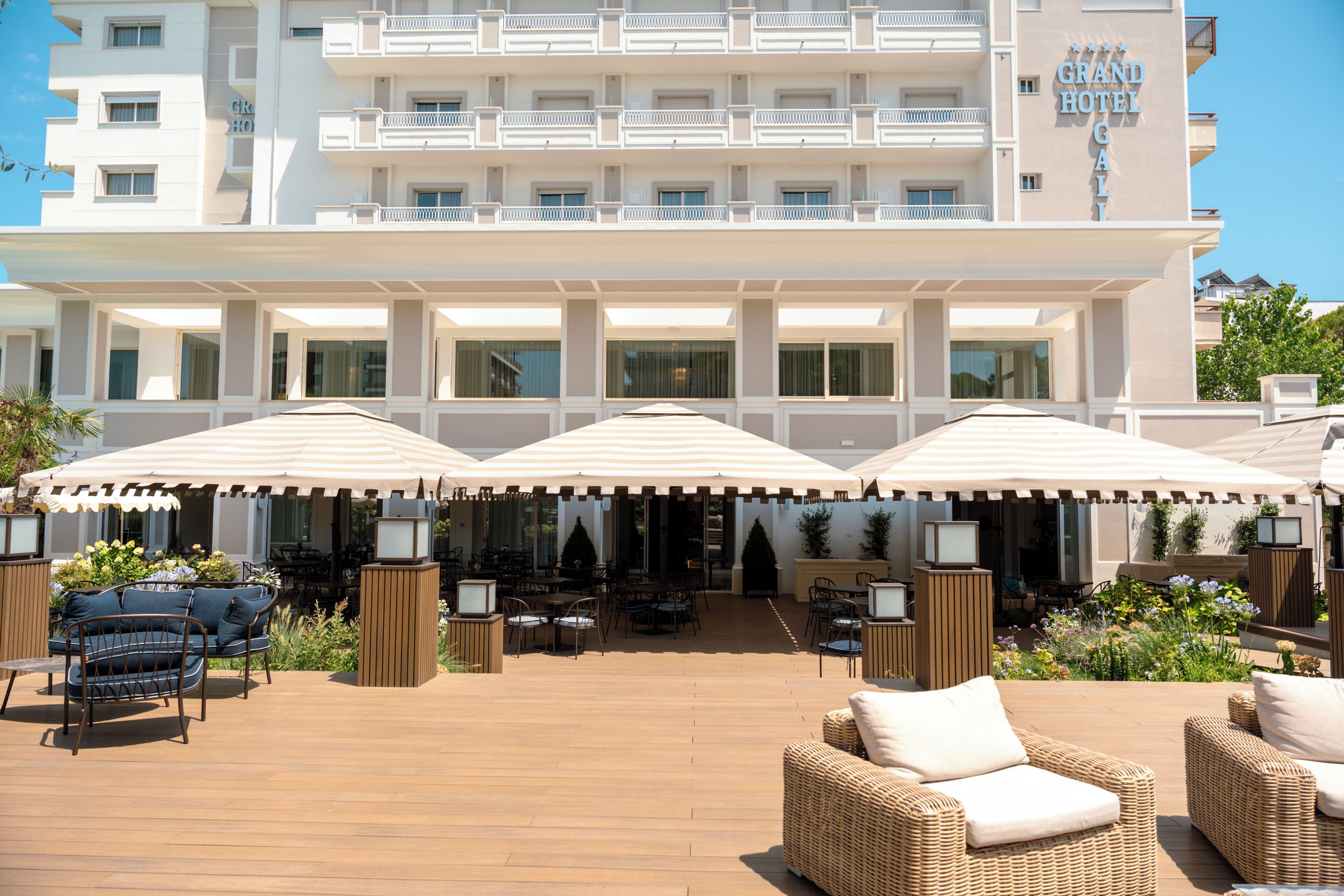 A hotel with a covered outdoor seating area featuring wicker furniture and umbrellas.