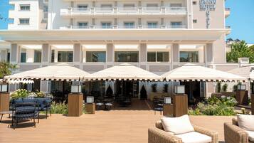 A hotel with a covered outdoor seating area featuring wicker furniture and umbrellas.