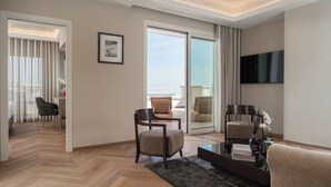A modern hotel room with a large sliding glass door leading to a balcony, a flat-screen TV mounted on the wall, and a seating area with a coffee table. - Grand Hotel Gallia (Cervia)