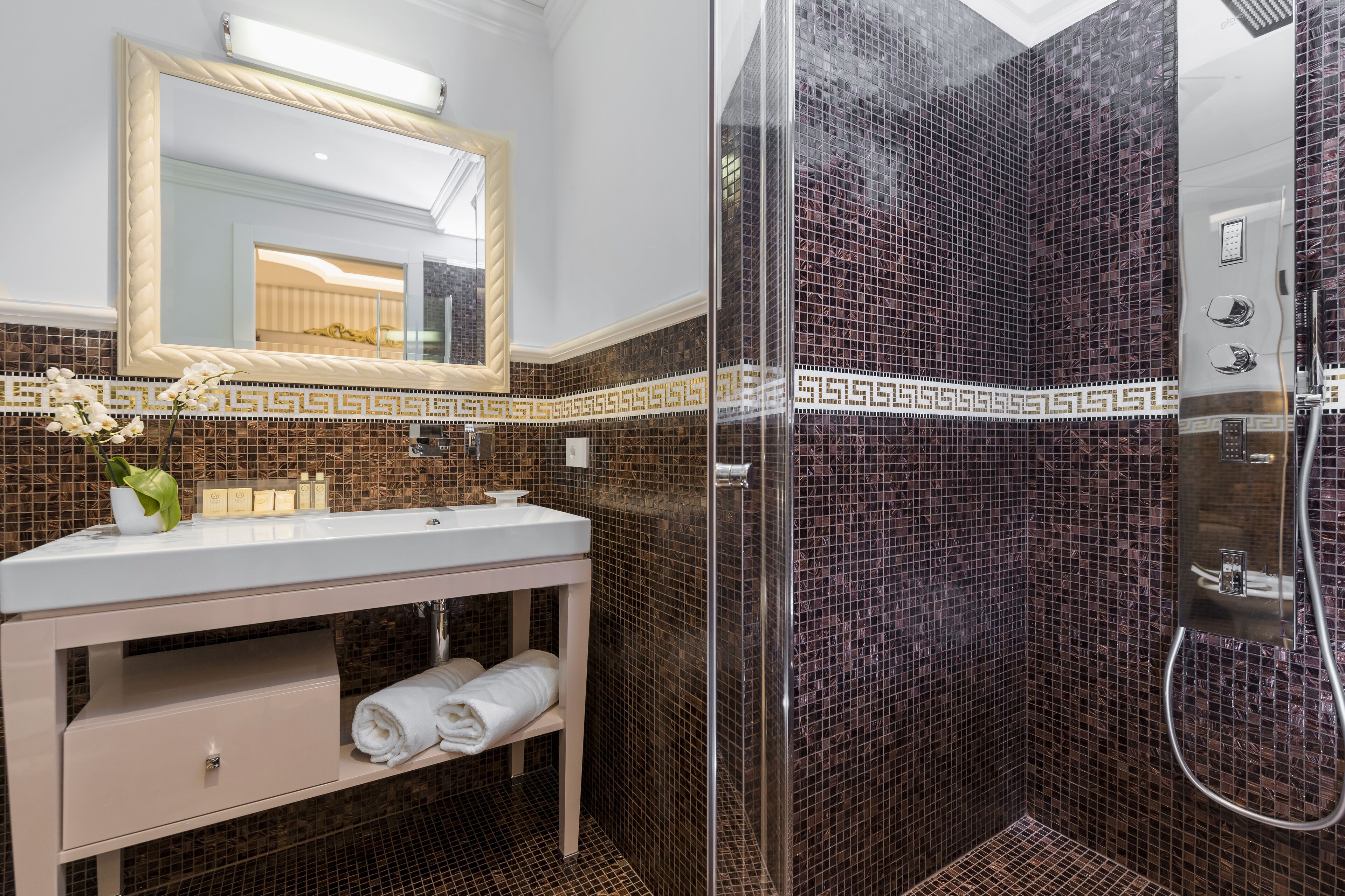 A bathroom with a white sink, a mirror, and a shower area with mosaic tiles.