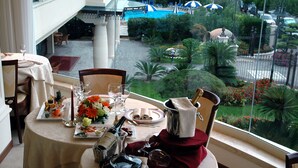 A dining table set for two with a view of a landscaped garden and pool. - Grand Hotel Gallia (Cervia)