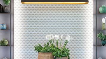 Un espace d’accueil moderne avec un comptoir en marbre, deux plantes en pot et un mur décoré d’un motif.