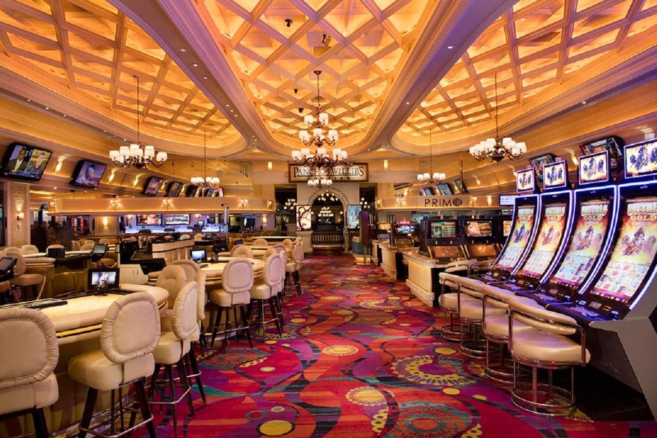 Interior de un casino con máquinas tragamonedas, zona de bar y asientos.