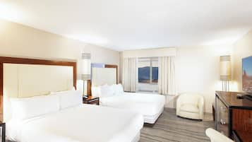 A hotel room with two beds, a desk, a chair, and a view of the mountains.