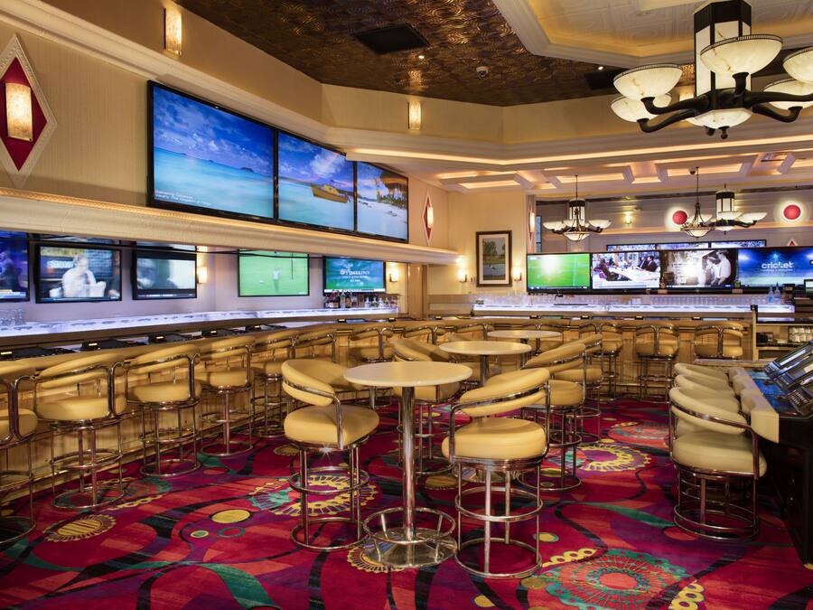 A bar area with multiple screens, bar stools, and a patterned carpet.