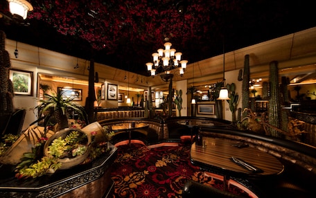 A dimly lit interior with a central round table, seating arrangements, and a ceiling adorned with artificial red flowers.