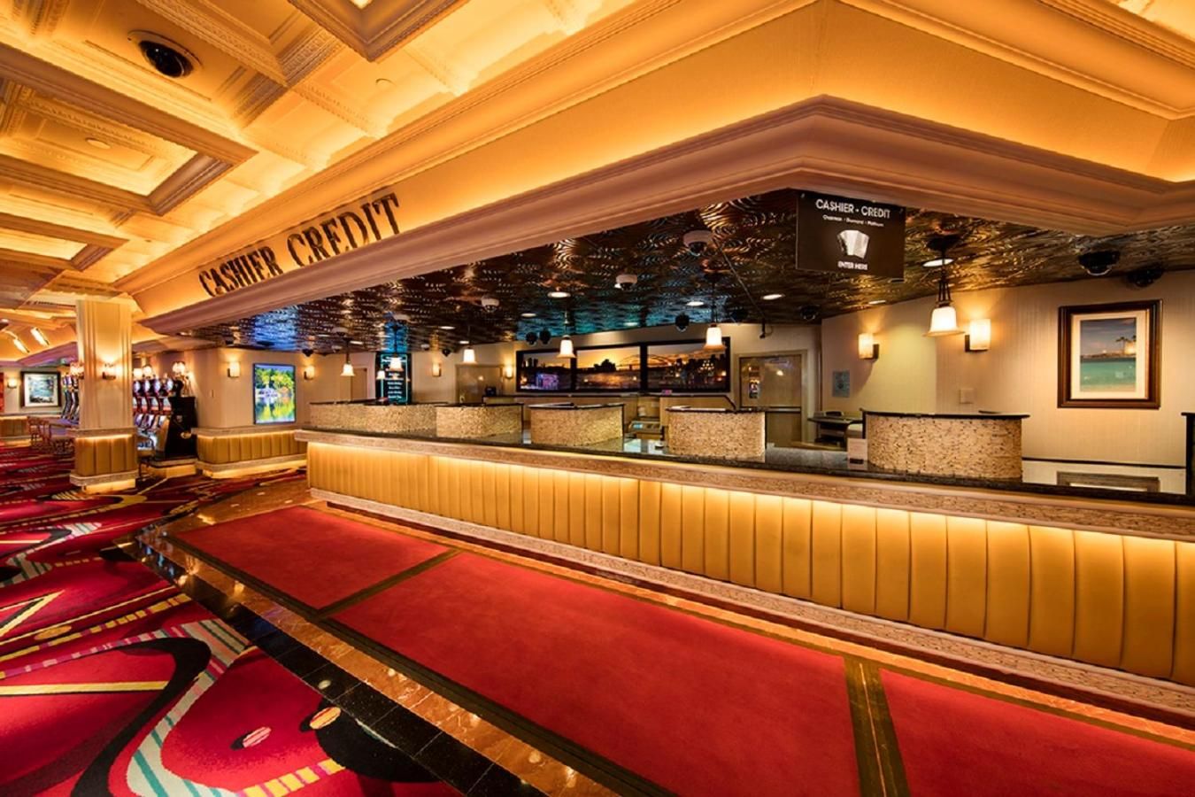 A hotel lobby with a cashier area, red carpeted seating, and a ceiling with intricate designs.