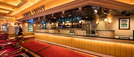 A hotel lobby with a cashier area, red carpeted seating, and a ceiling with intricate designs.