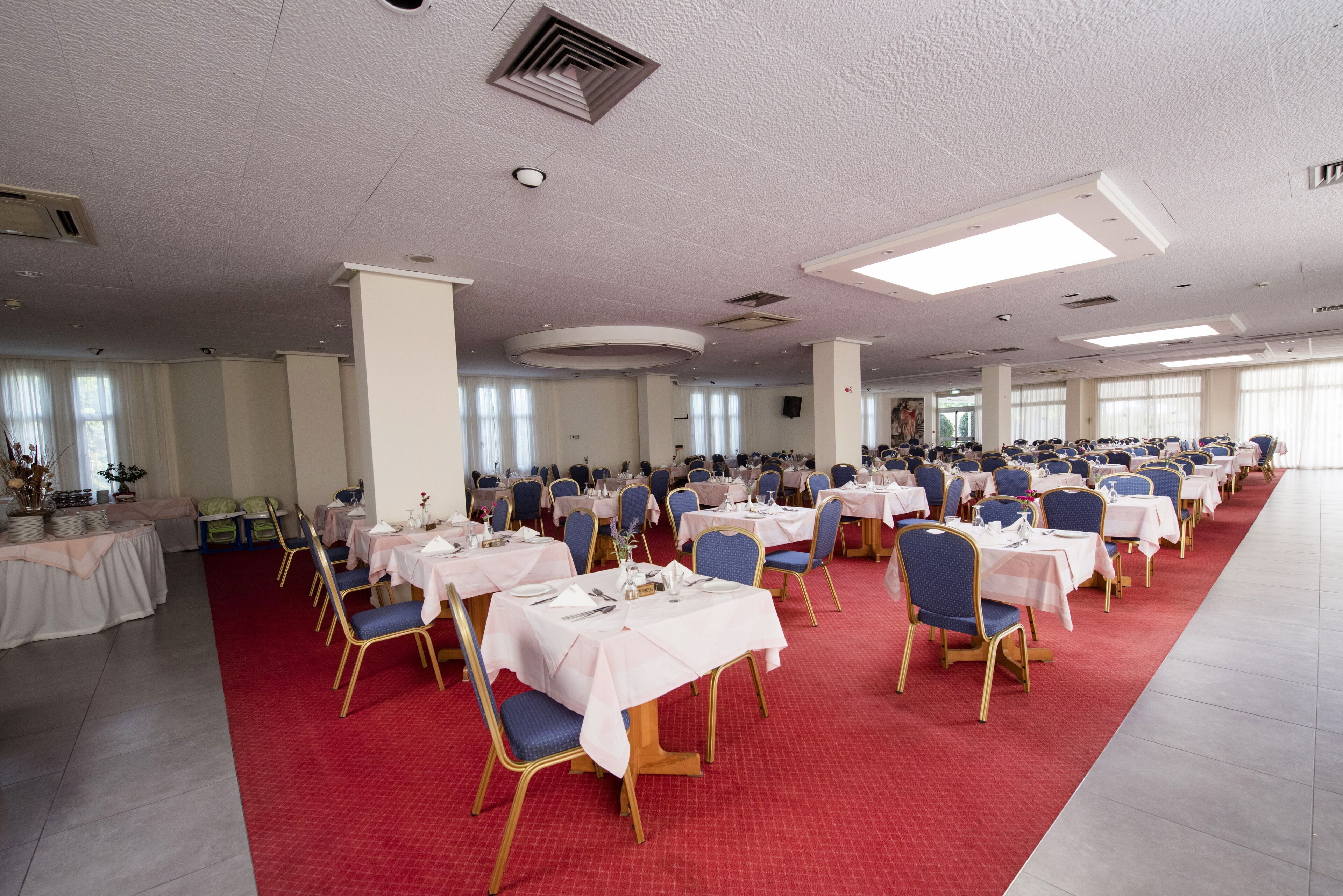 A banquet hall with round tables, chairs, and a red carpet.