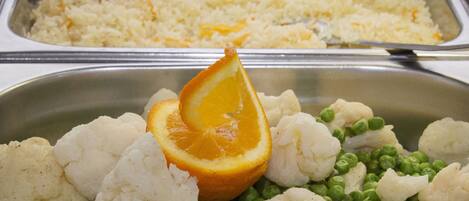 Un bufé con diversos platos, incluyendo arroz, coliflor, guisantes y una rodaja de naranja.