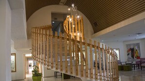 Una escalera de caracol con barandillas de madera y lámparas esféricas colgantes en un vestíbulo amplio con techo alto y suelos pulidos.