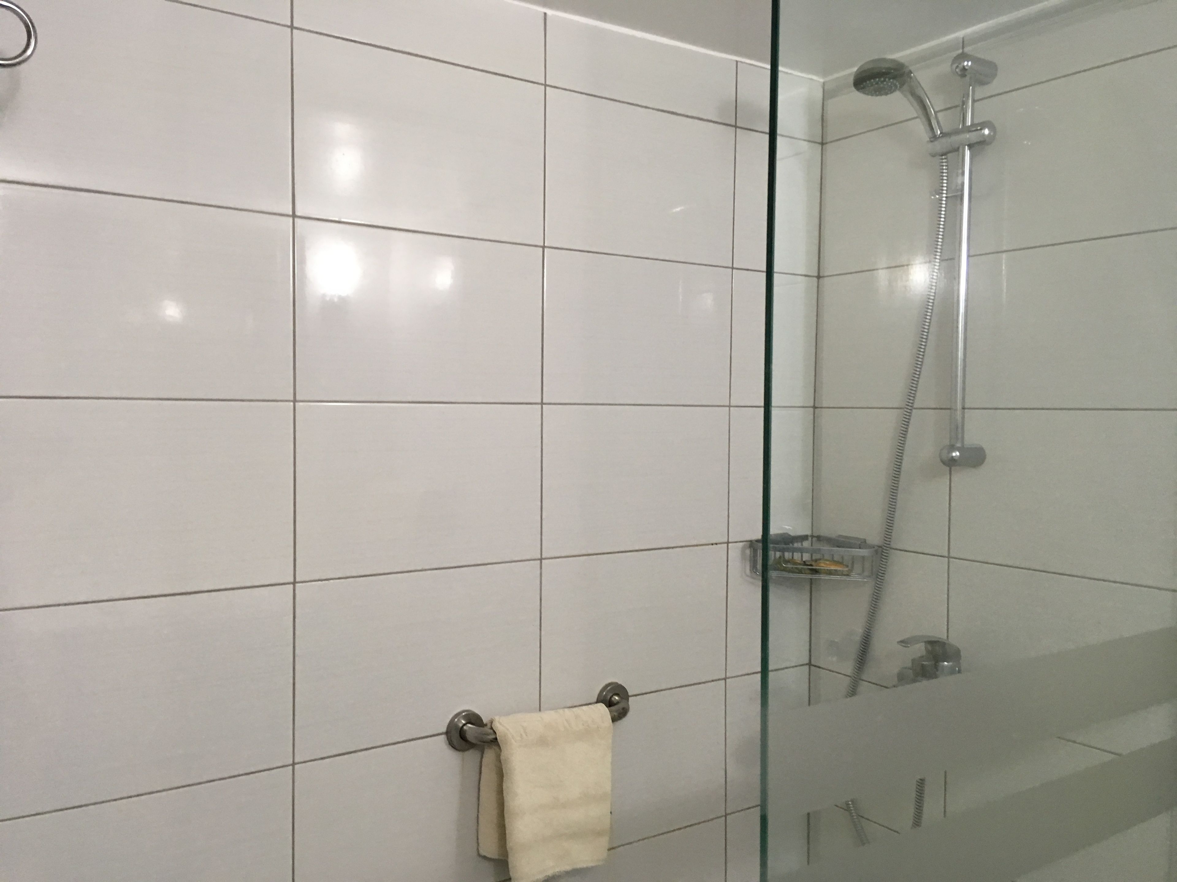 Une salle de bain moderne avec des carreaux blancs, une douche en verre et un porte-serviettes.