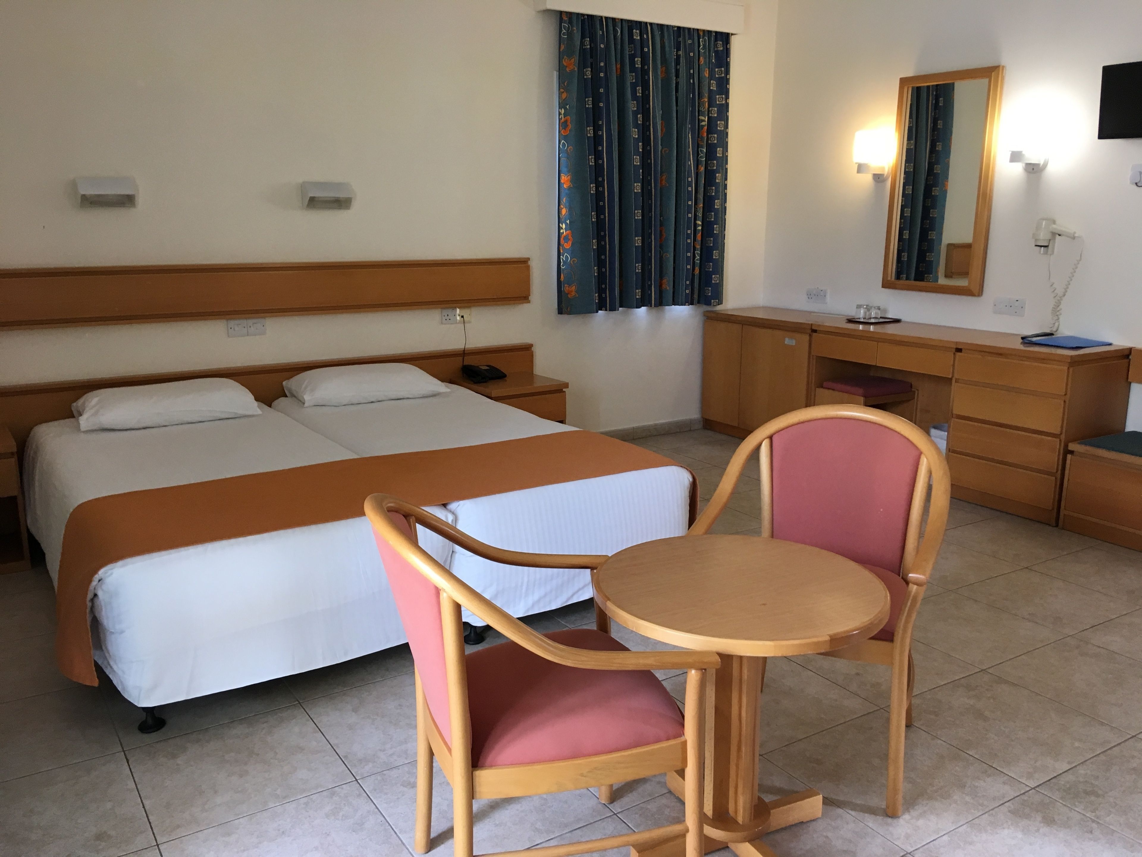 A hotel room with two beds, a desk, a chair, a mirror, and a window with curtains.